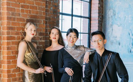 Terra Quartet, three women and one man standing close together against a brick wall and window.