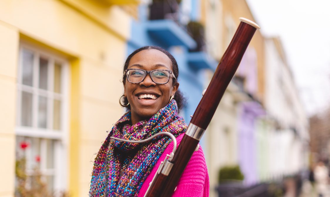 Woman with black hair and glasses smiling while holding a bassoon.