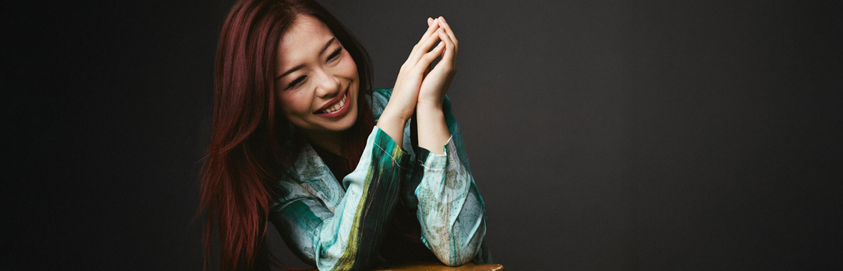 Junyan Chen, woman with long dark hair sitting with her hands together and smiling.