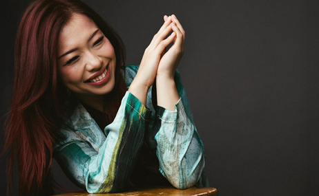 Junyan Chen, woman with long dark hair sitting with her hands together and smiling.