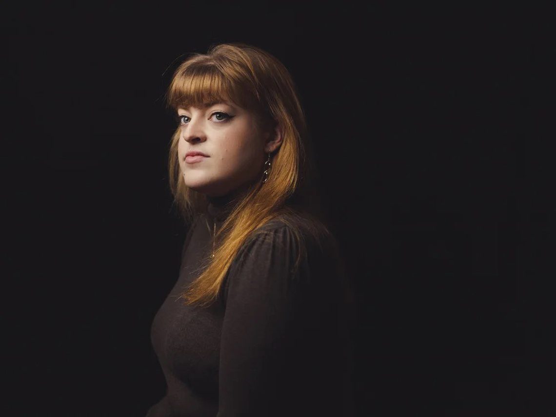 Young woman with long red hair, outlined in black against a black background.