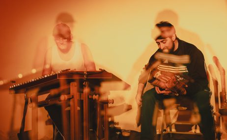 Blurry image of two men playing musical instruments.