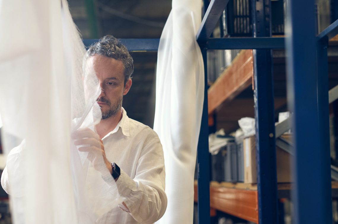 Man with short dark hair wearing a white shirt, arranging a hanging sheet.
