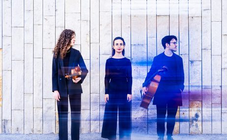 Trio Archai, one man and two women, all wearing dark clothing and holding musical instruments against a stone wall.