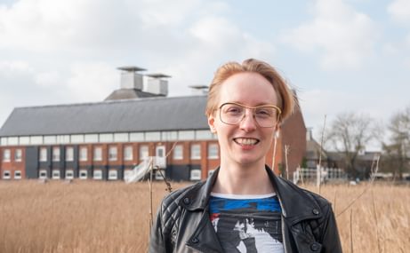 woman with short, fair hair and glasses, smiling at the camera, with a maltings concert hall building in the background.