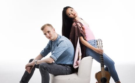 Woman with long black hair and man with short blond hair standing back to back.