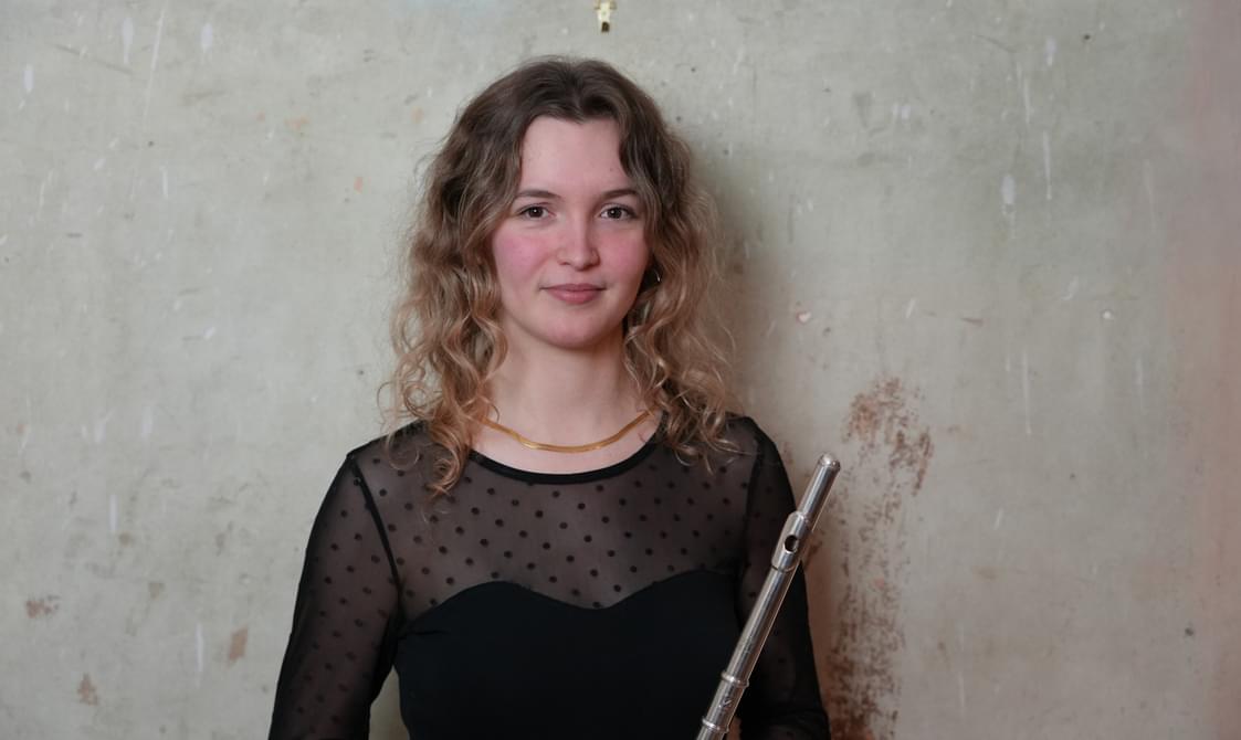 Woman with long curly hair holding a flute and smiling at the camera.