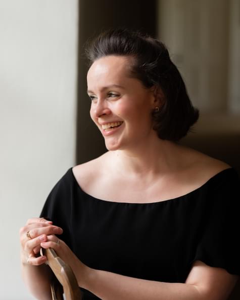 Woman with bobbed dark hair looking out of a window and smiling.