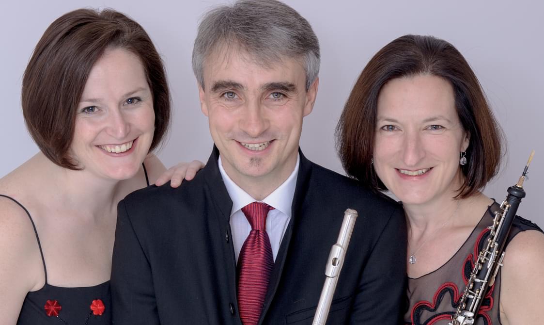 Man and two women standing together holding wind instruments and smiling.