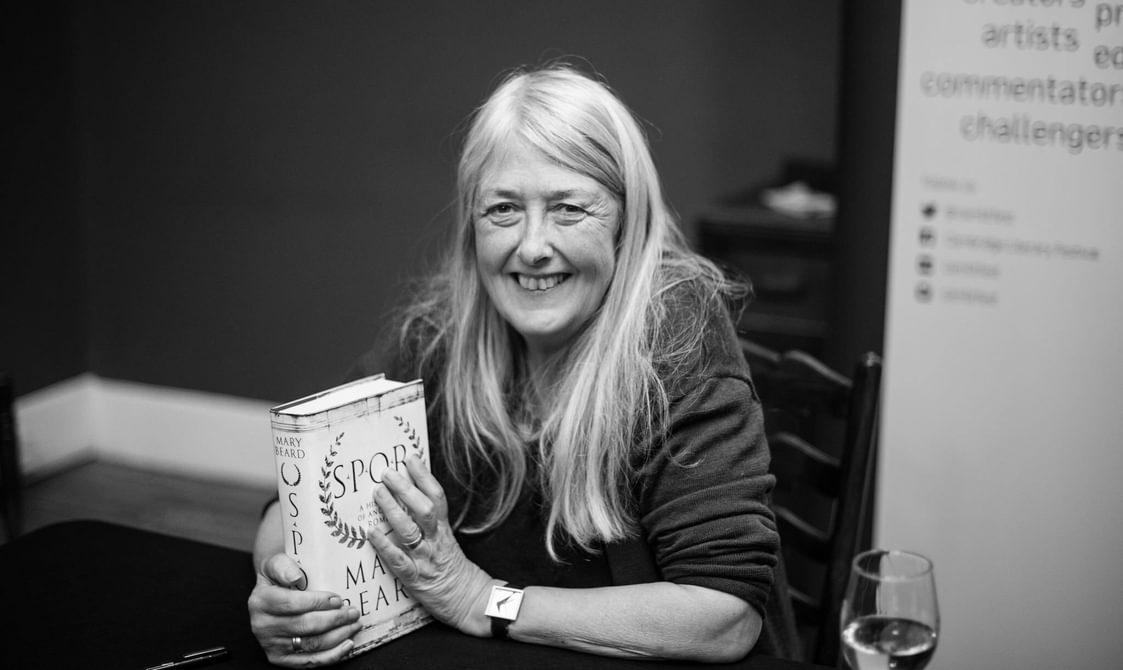 Mary Beard smiling and holding her SPQR book