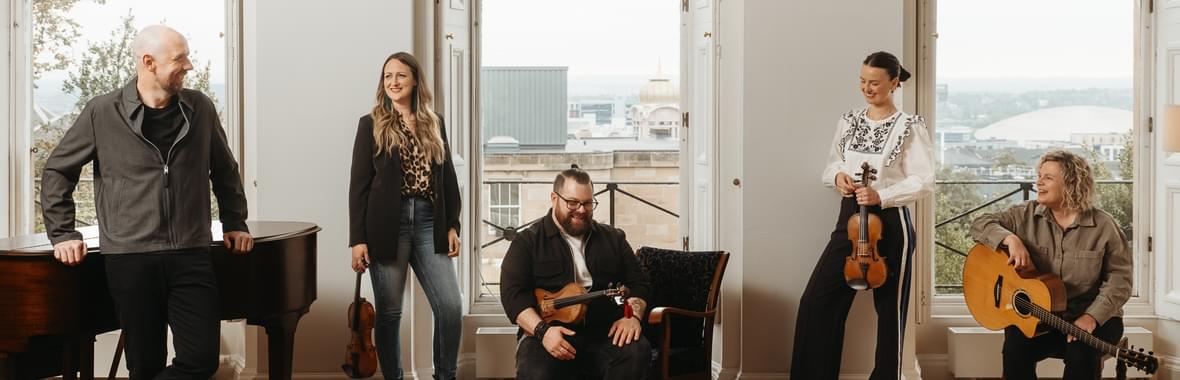 Group of musicians standing in a room with their instruments and smiling.