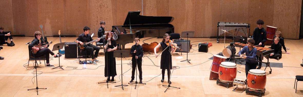 Young people onstage singing and playing intruments.