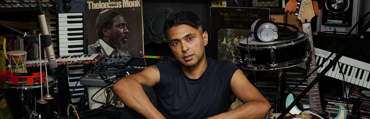 Man sitting in a room surrounded by musical instruments.