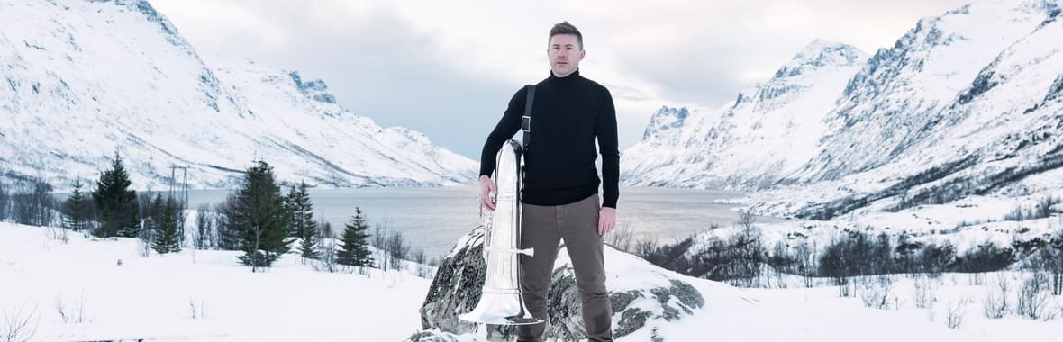Man standing amidst a snowy landscape holding a tuba instrument.