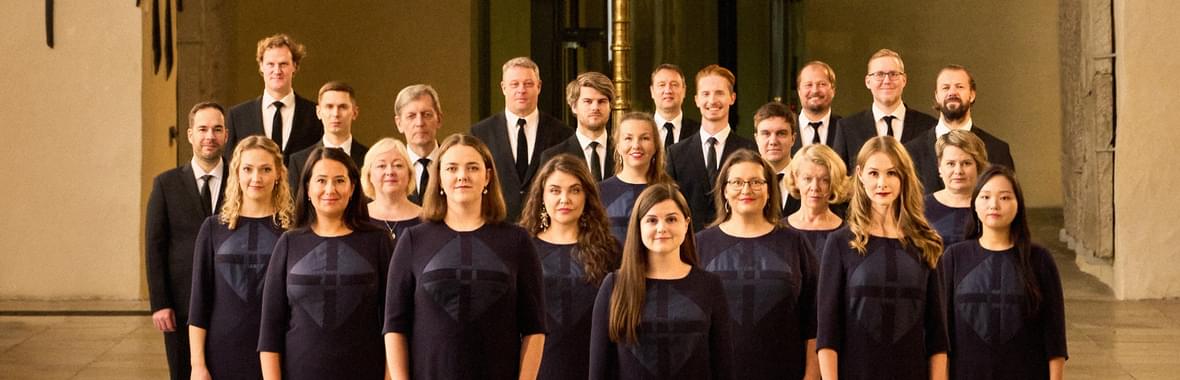 Group of women and men dressed in black, standing beneath an ornate church chandelier.
