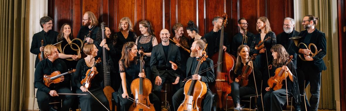 Group of musicians wearing black and holding their instruments standing and sitting in front of old wooden doors.