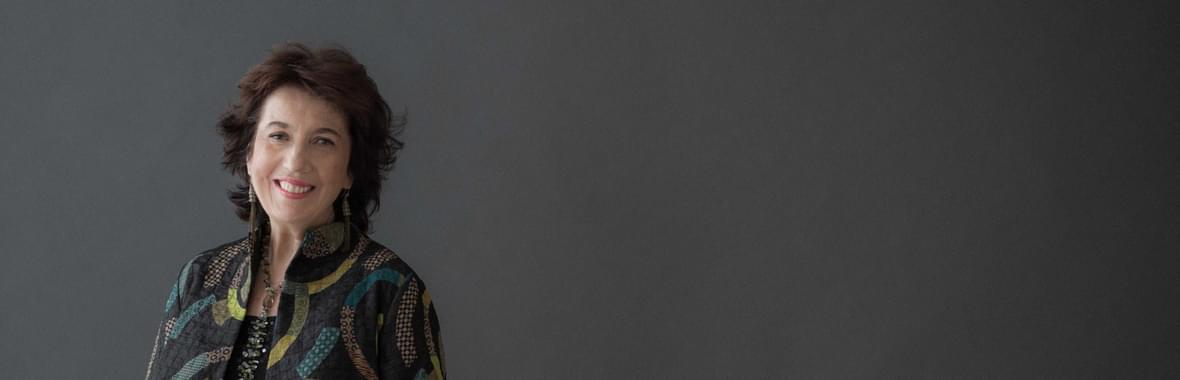 Woman with short brown hair wearing a multi-coloured jacket and smiling.