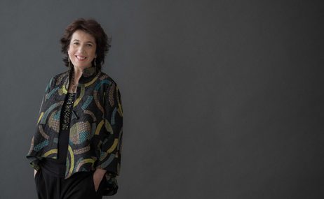 Woman with short brown hair wearing a multi-coloured jacket and smiling.