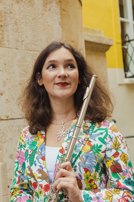 Woman with brown curly hair holding a flute and smiling.