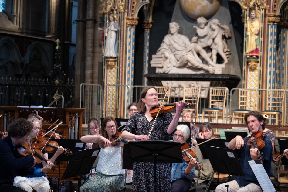 Woman playing the violin surrounded by musicians in the setting of an ornate church.