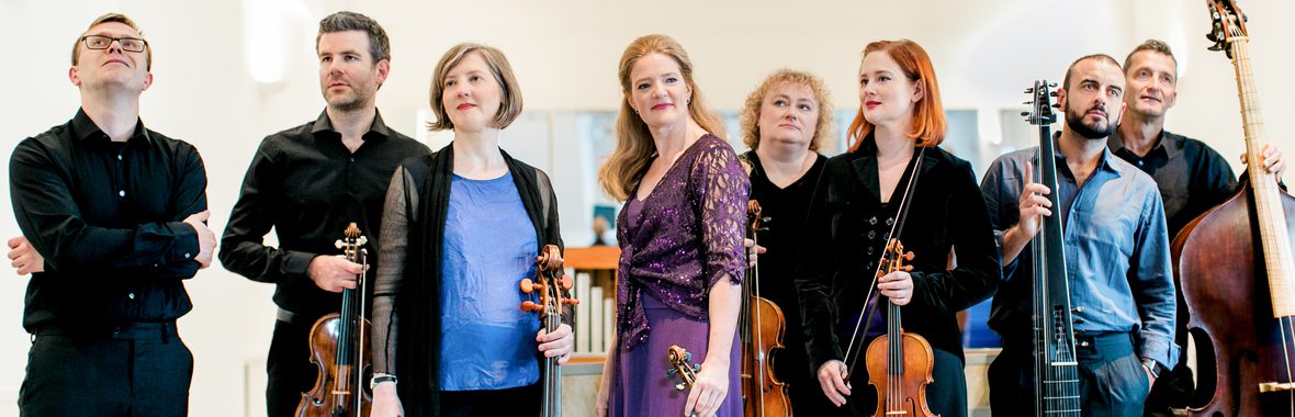 Group of male and female musicians holding instruments and standing against a white background.