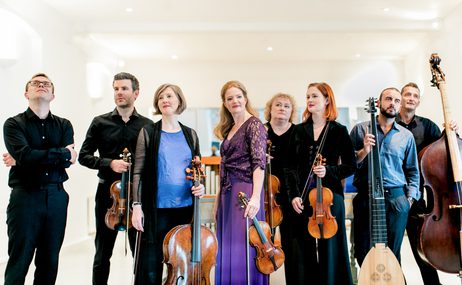 Group of male and female musicians holding instruments and standing against a white background.