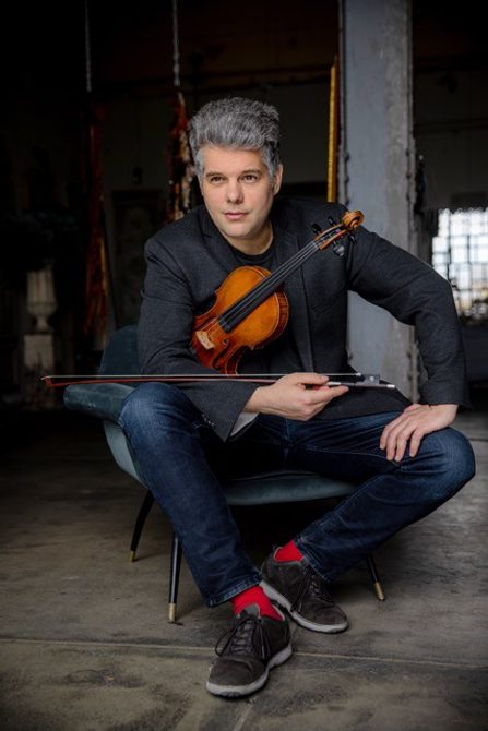 Man with short grey hear sitting holding a violin.