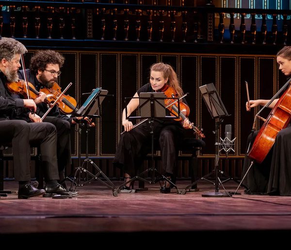 String Quartet of two men and two women playing string instruments on a wooden stage.