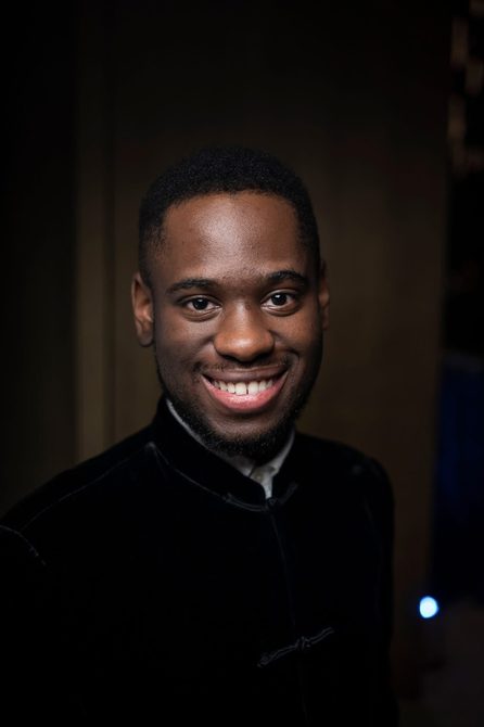 Close-up up of Black man wearing a black jacket and smiling.