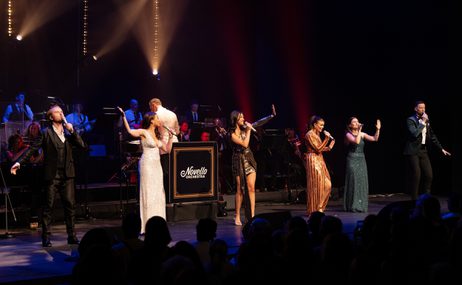 Singers onstage performing in front of an orchestra.