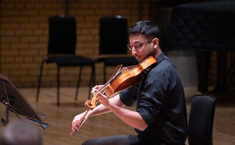 Man with short dark hair playing a string instrument.