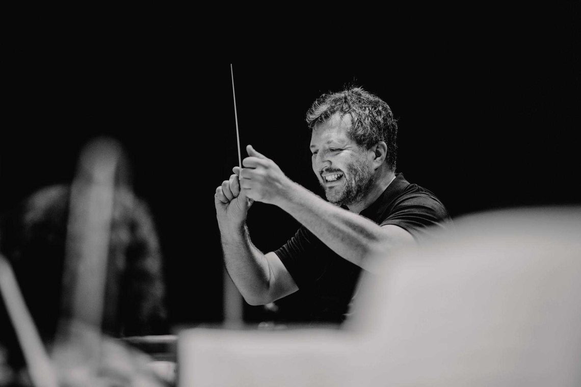 Man conducting an orchestra and smiling.