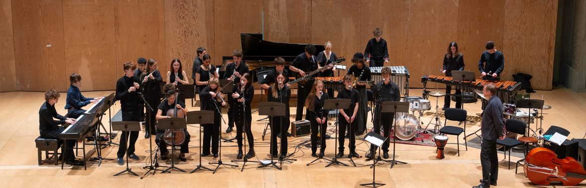 Group of young musicians standing on a stage playing musical instruments and singing in front of an audience.