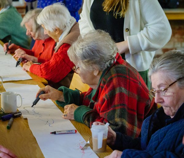 A group of people writing on one sheet of paper with coloured pens