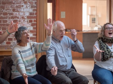 Four people sat on chairs, singing and gesturing.