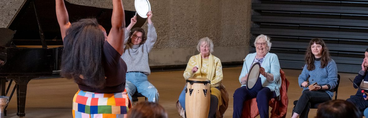A group of people playing instruments facing someone who is raising their hands.