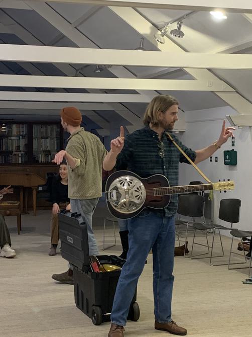 Man with a guitar conducting.