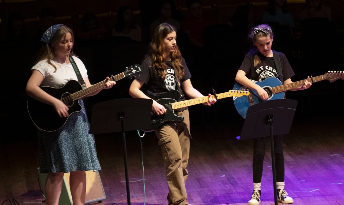 Three older girls playing guitars onstage.