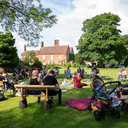 Children accompanied by adults in a garden, circled by benches and prams.