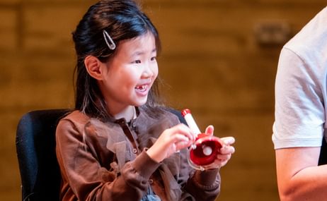 Young girl sitting smiling and holding a musical instrument
