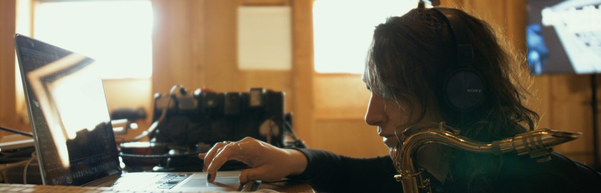 A person holding a saxophone in one hand and typing with the other