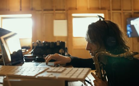 A person holding a saxophone in one hand and typing with the other