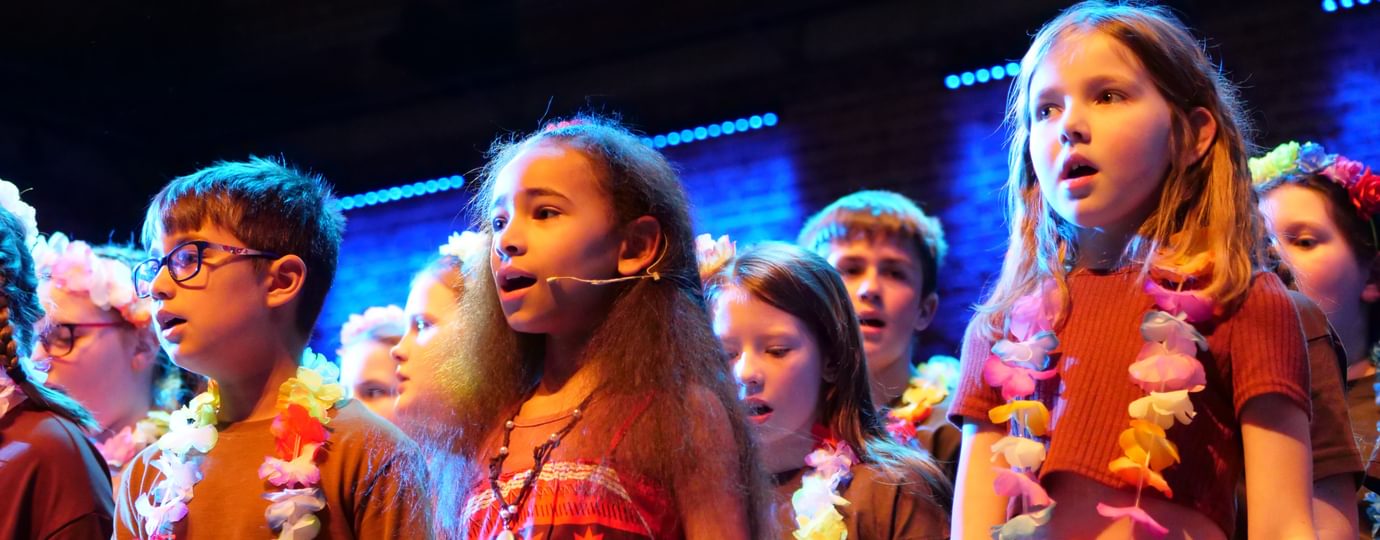 Group of children singing while wearing colourful clothes and chains of flowers.