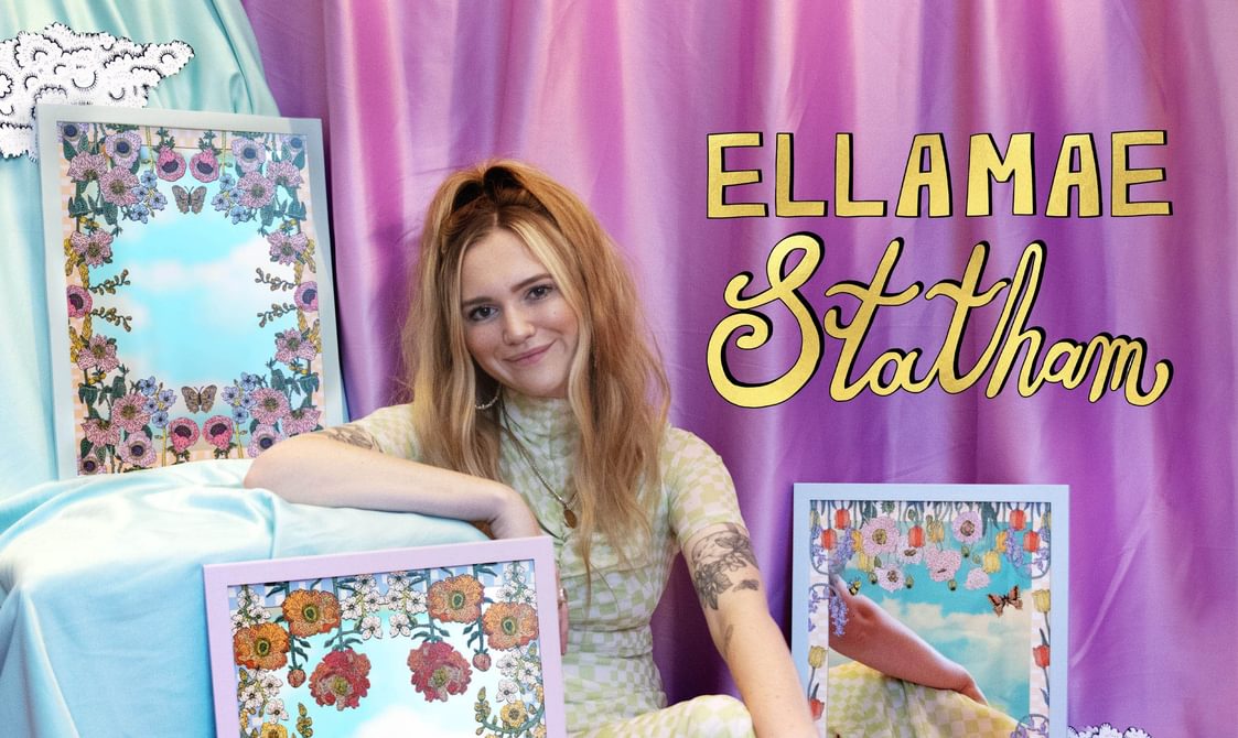 Woman with long blond hair sitting on the floor surrounded by artworks and smiling.