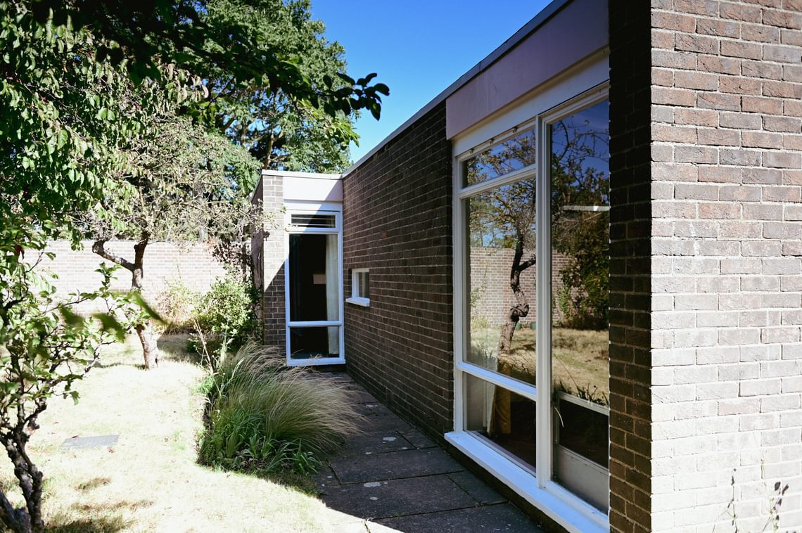 Exterior view of small bungalow, shaded by a tree