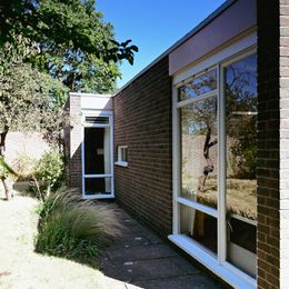 Exterior view of small bungalow, shaded by a tree