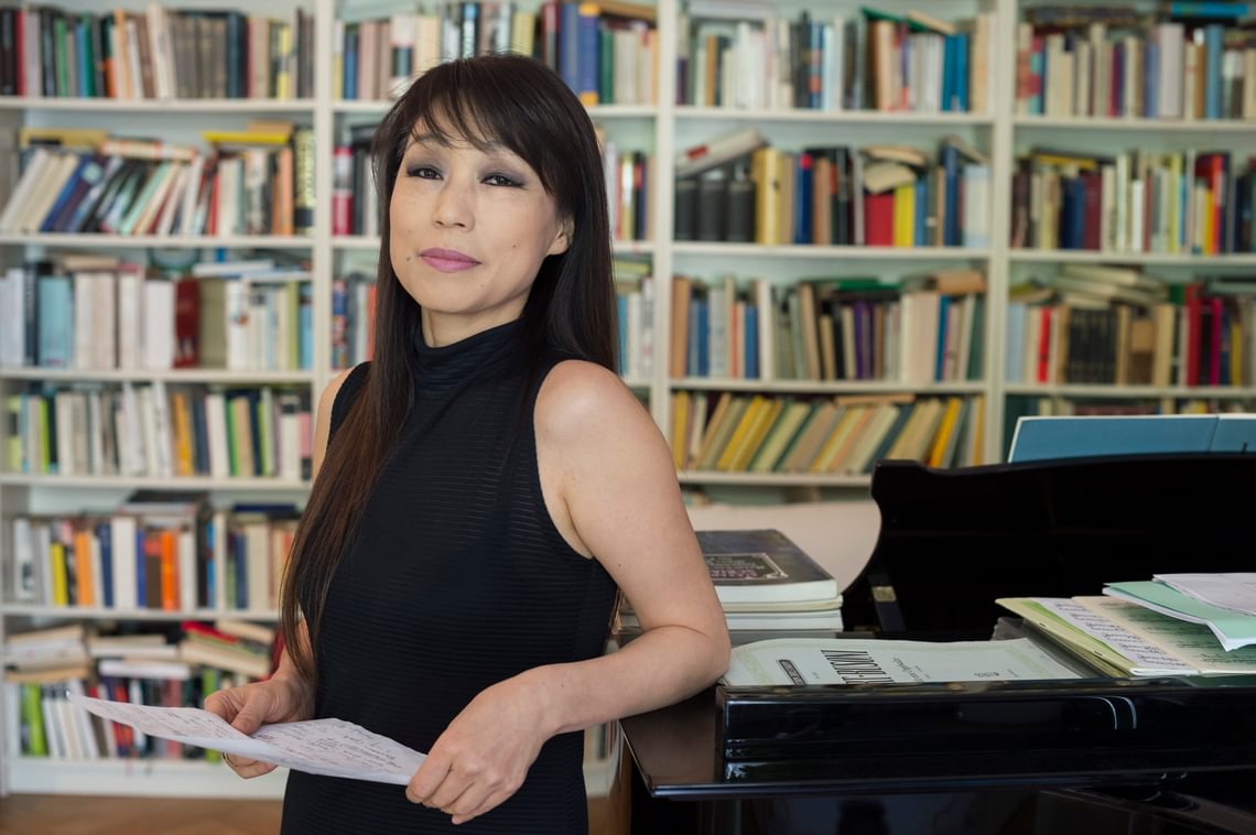 Woman leaning against a piano with bookshelves in the background