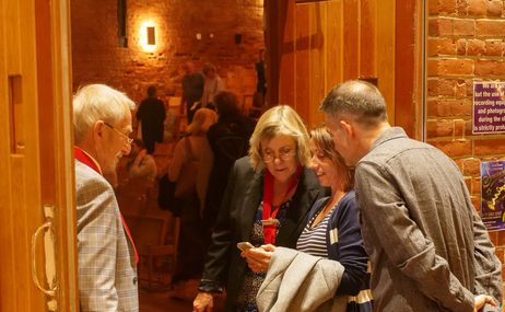 man and woman standing at the entrance to a concert hall, looking at tickets on a phone being shown by male and female guests