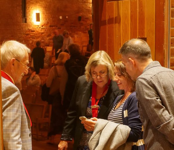 man and woman standing at the entrance to a concert hall, looking at tickets on a phone being shown by male and female guests