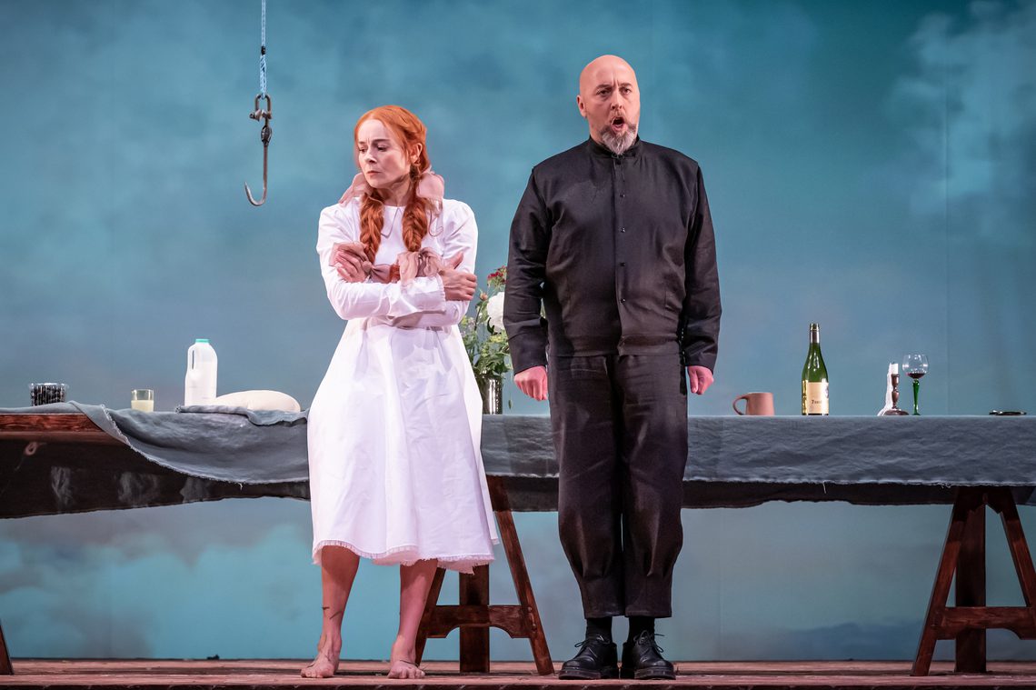 A women dressed in a night gown standing cross armed next to a man in a black suit singing.